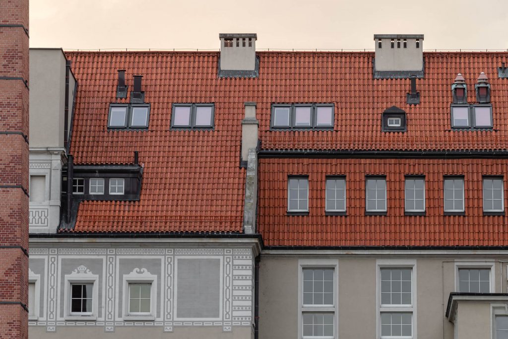 A red tiled roof featuring windows and a clock, showcasing a charming architectural detail.